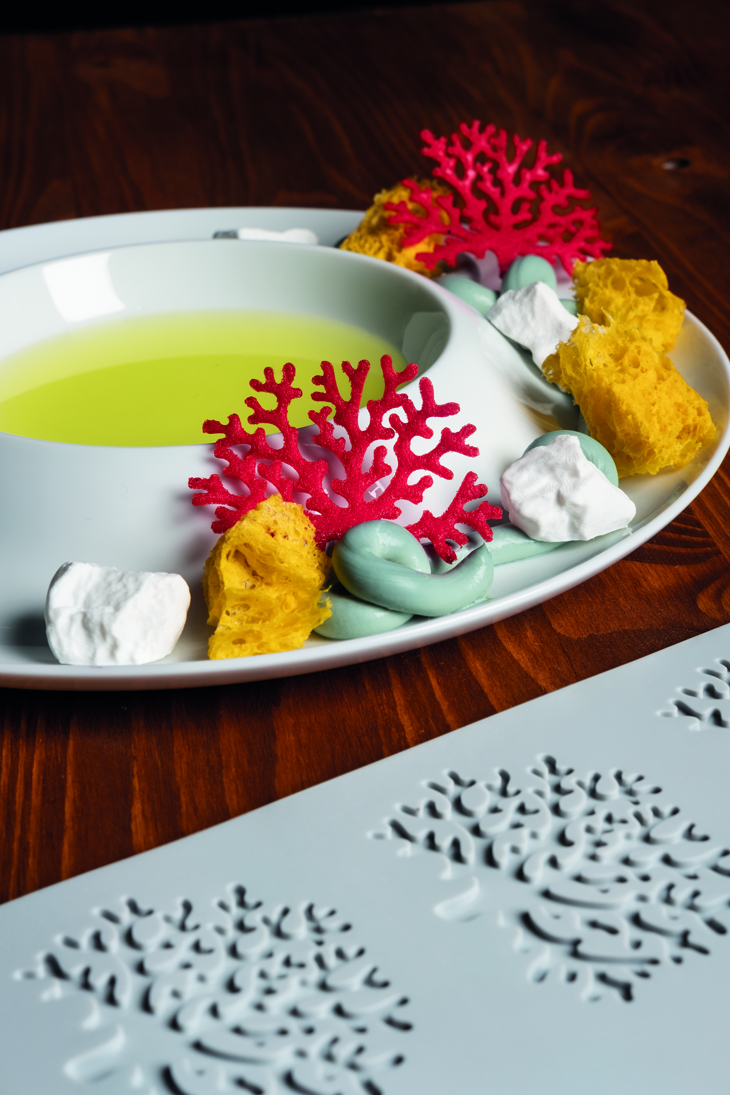 dekorierter weißer Suppenteller mit roten Korallenformen aus Silikonform Korallen, auf Holztisch, Silikonform Korallen im Vordergrund