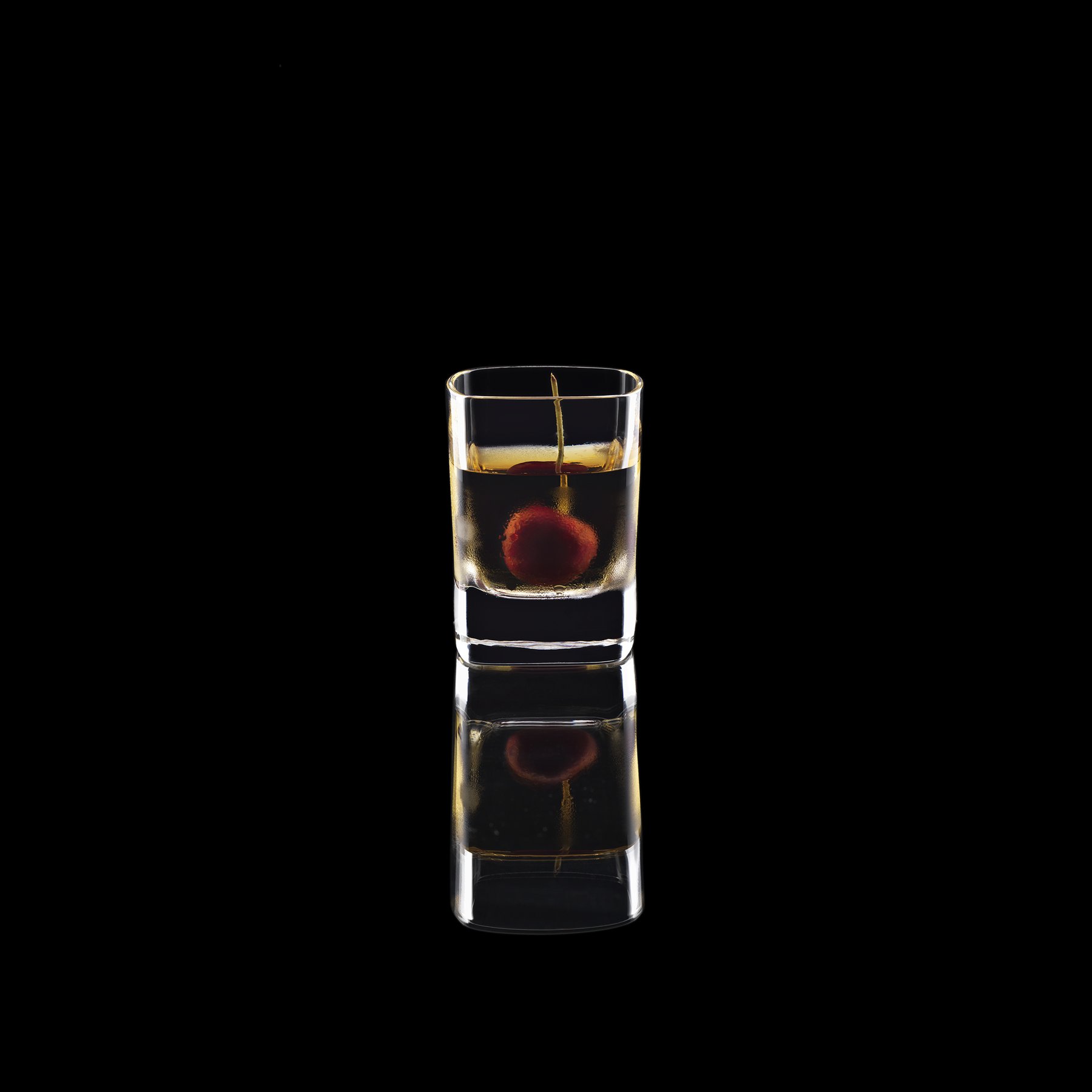 Likörglas mit Alkohol und einer Cocktailkirsche gefüllt vor schwarzem Hintergrund
