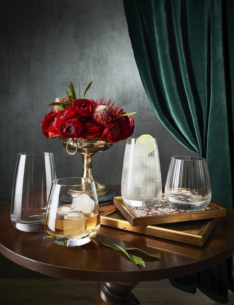 Whiskyglas, Longdrinkglas  jeweils mit Eis und Alkohol gefüllt, 2 leere Gläser Serie Mixology Classic Club Beverage, 510 ml,  alles auf kleinem elegantem Holzbistrotisch mit  Rosenschale  
